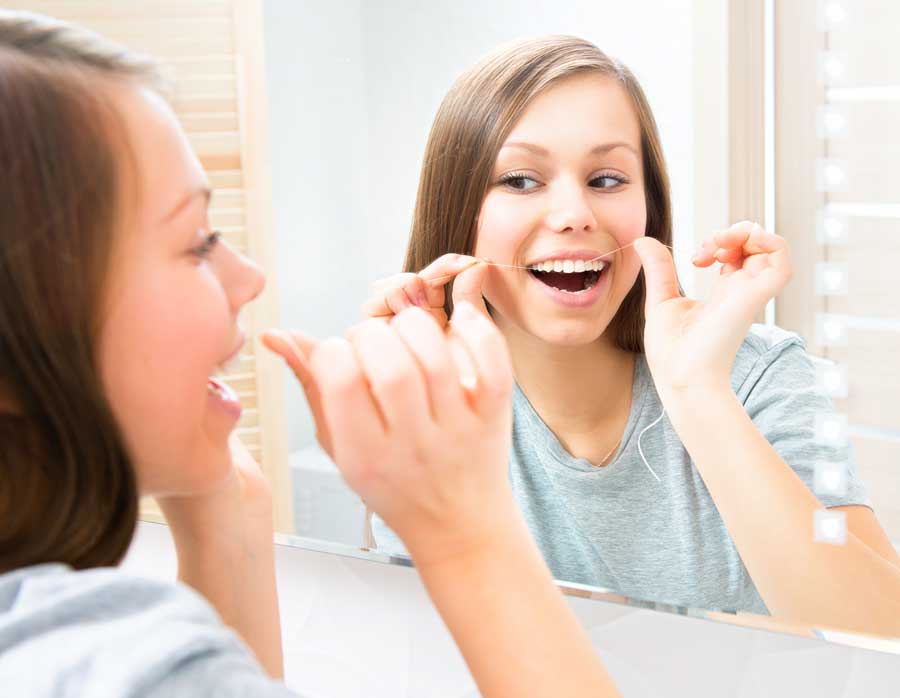 young woman flosses teeth in front of mirror